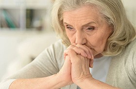 Sad senior woman clasping her hands near her mouth