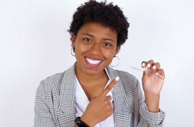 Smiling woman pointing at her Invisalign aligner