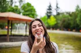 Woman standing outside next to fountain, holding clear aligner