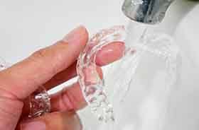 Hand holding clear aligner under bathroom faucet