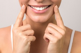 Woman pointing at her beautiful smile, which contains tooth-colored fillings