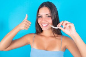 Young woman holding Invisalign aligner and making thumbs-up gesture
