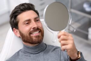 Happy male dental patient holding hand mirror